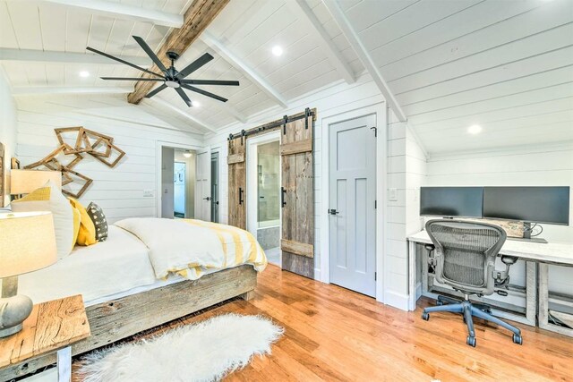bedroom featuring wood walls, a barn door, wood finished floors, vaulted ceiling with beams, and ensuite bath