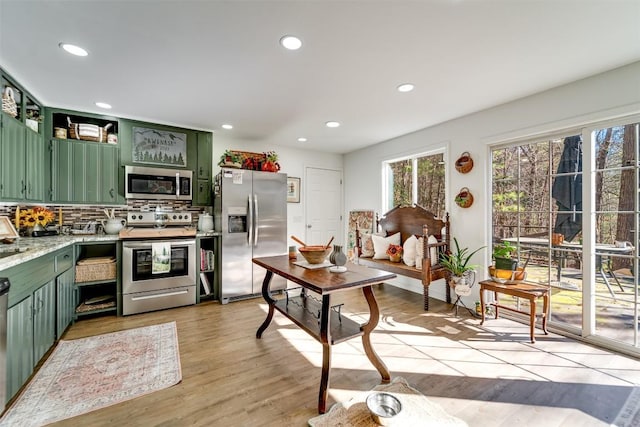 kitchen with light hardwood / wood-style flooring, appliances with stainless steel finishes, tasteful backsplash, light stone countertops, and green cabinetry