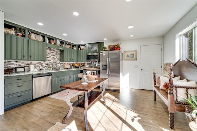 kitchen with sink, light hardwood / wood-style flooring, green cabinets, stainless steel appliances, and decorative backsplash