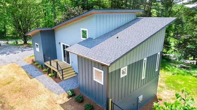 view of side of property with roof with shingles, board and batten siding, and view of scattered trees