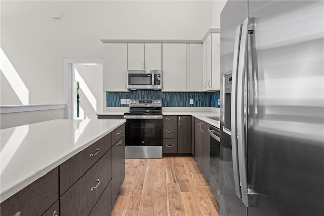 kitchen featuring stainless steel appliances, light countertops, white cabinetry, light wood-style flooring, and dark brown cabinetry