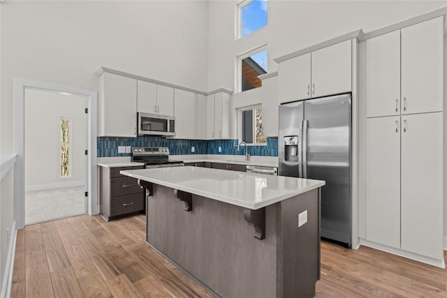kitchen with appliances with stainless steel finishes, a towering ceiling, light wood-style floors, light countertops, and a breakfast bar
