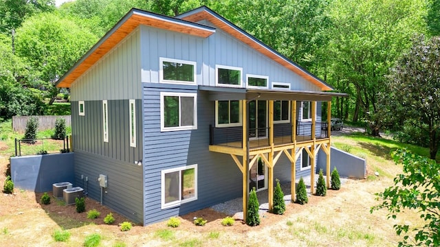 rear view of house with board and batten siding, central AC, and fence