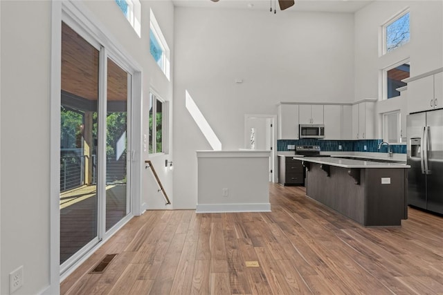 kitchen with appliances with stainless steel finishes, a high ceiling, a kitchen island, light countertops, and a kitchen bar