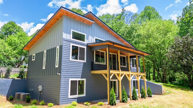 back of property featuring board and batten siding, a balcony, ceiling fan, fence, and cooling unit