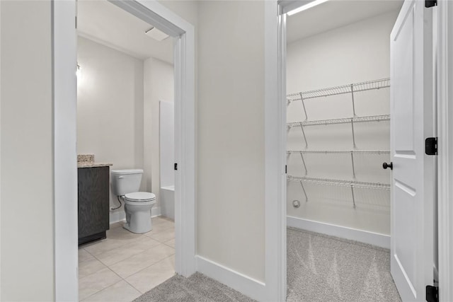 bathroom with toilet, a walk in closet, baseboards, a bath, and tile patterned flooring
