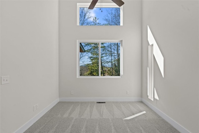 carpeted spare room featuring baseboards, a towering ceiling, and a ceiling fan
