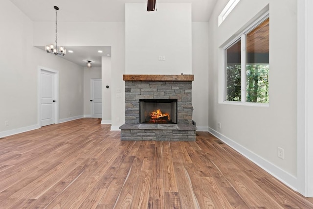 unfurnished living room with wood finished floors, a fireplace, a chandelier, baseboards, and a towering ceiling