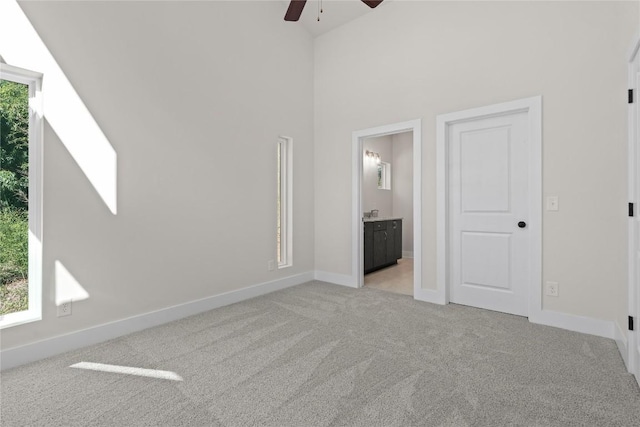 unfurnished bedroom with light carpet, a high ceiling, baseboards, ensuite bath, and ceiling fan
