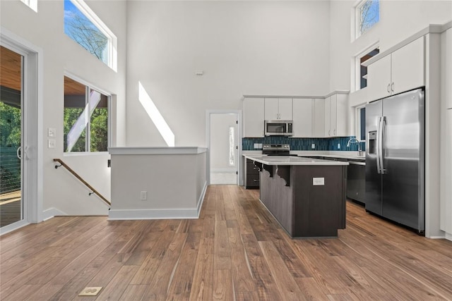 kitchen featuring stainless steel appliances, a towering ceiling, a center island, light countertops, and white cabinetry