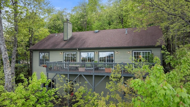 rear view of property featuring a chimney, a wooden deck, and a shingled roof