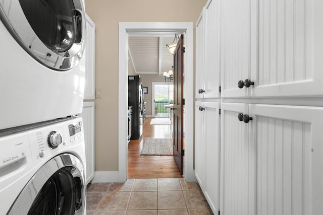 laundry room with stacked washing machine and dryer, cabinet space, ornamental molding, and baseboards