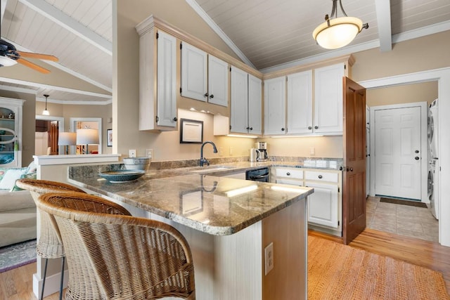 kitchen with stacked washer / drying machine, a peninsula, a kitchen bar, hanging light fixtures, and wooden ceiling
