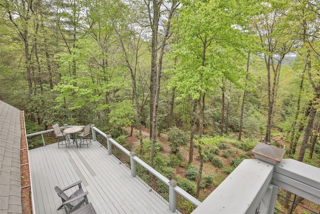 wooden deck with a forest view and outdoor dining space