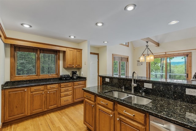 kitchen with light wood-type flooring, brown cabinets, a sink, dark stone countertops, and dishwasher