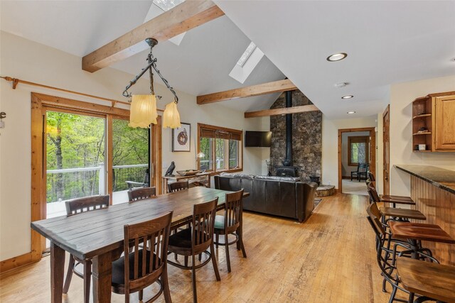 dining area with a wood stove, vaulted ceiling with skylight, recessed lighting, baseboards, and light wood-type flooring