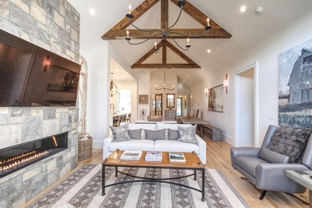 living area with wood finished floors, baseboards, high vaulted ceiling, a fireplace, and a notable chandelier