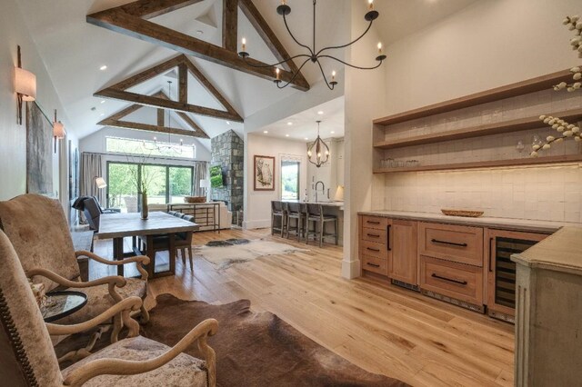 dining space with a chandelier, high vaulted ceiling, light wood-style floors, beverage cooler, and beam ceiling