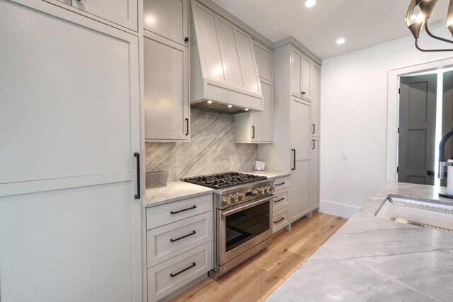 kitchen featuring light wood finished floors, custom exhaust hood, recessed lighting, high end stainless steel range, and tasteful backsplash