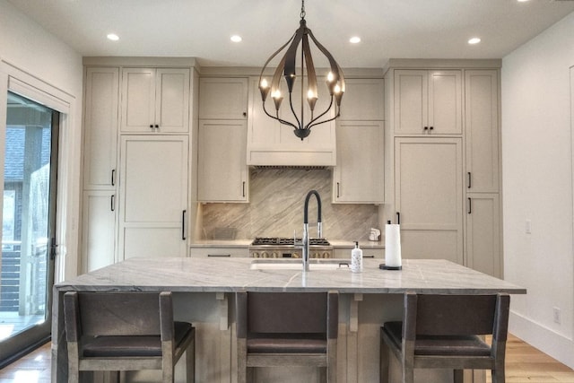 kitchen featuring gray cabinetry, tasteful backsplash, light wood-style floors, baseboards, and light stone countertops