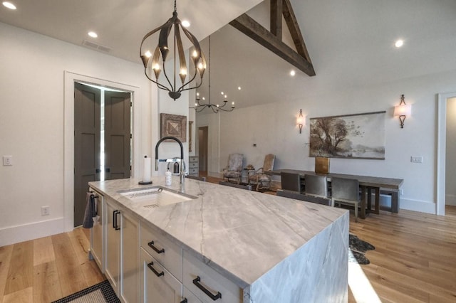 kitchen with a sink, a chandelier, white cabinetry, light stone countertops, and light wood-style flooring
