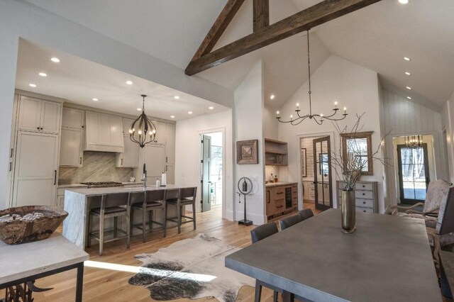 kitchen featuring backsplash, light wood-type flooring, a notable chandelier, and a kitchen island with sink