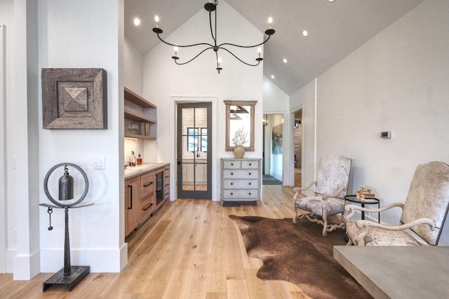 sitting room with light wood-style floors, high vaulted ceiling, beverage cooler, a chandelier, and baseboards