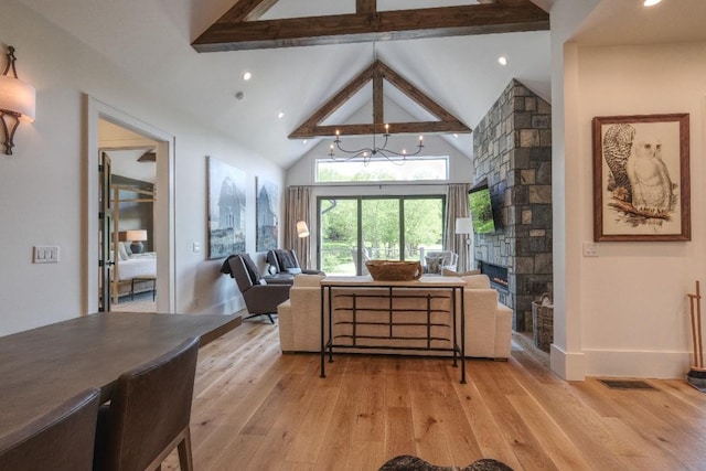 living room featuring beam ceiling, light wood-style flooring, a stone fireplace, high vaulted ceiling, and baseboards