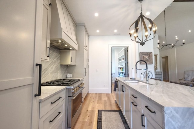 kitchen with light stone countertops, a sink, decorative backsplash, high end stove, and light wood-type flooring