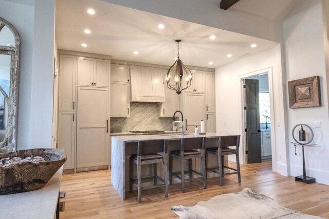 kitchen with a breakfast bar, a sink, decorative backsplash, light countertops, and light wood-style floors