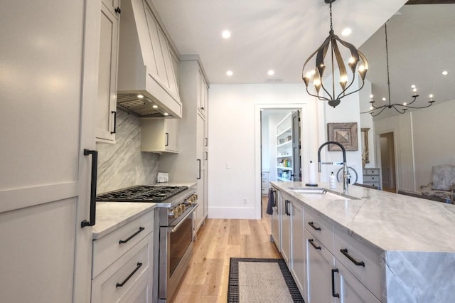 kitchen featuring stainless steel stove, a sink, premium range hood, a chandelier, and light wood finished floors
