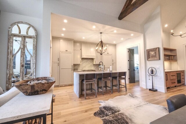 kitchen with an island with sink, decorative backsplash, light wood-style flooring, a kitchen breakfast bar, and a notable chandelier