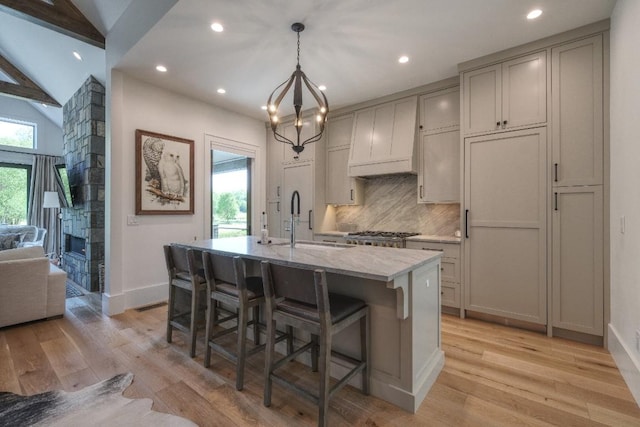 kitchen with a sink, a kitchen island with sink, decorative backsplash, a kitchen breakfast bar, and light wood-style flooring