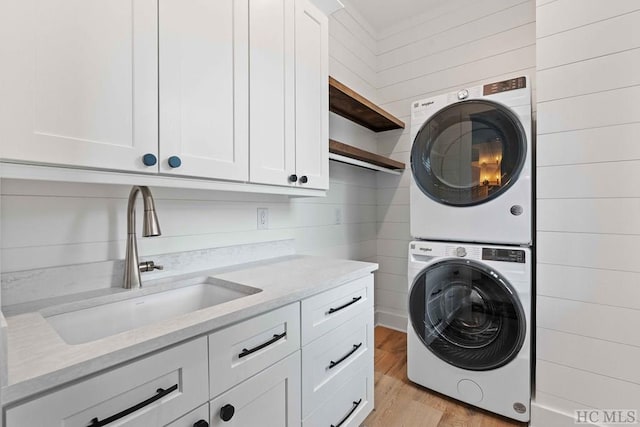 laundry area with sink, cabinets, wooden walls, and stacked washer and clothes dryer