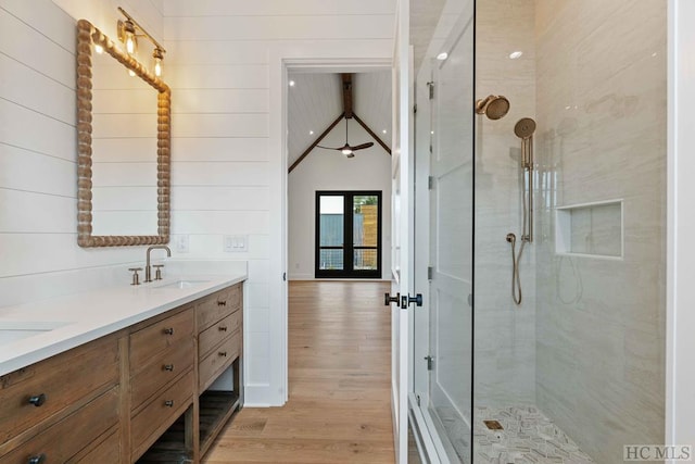 bathroom with a tile shower, hardwood / wood-style floors, wood walls, and vanity