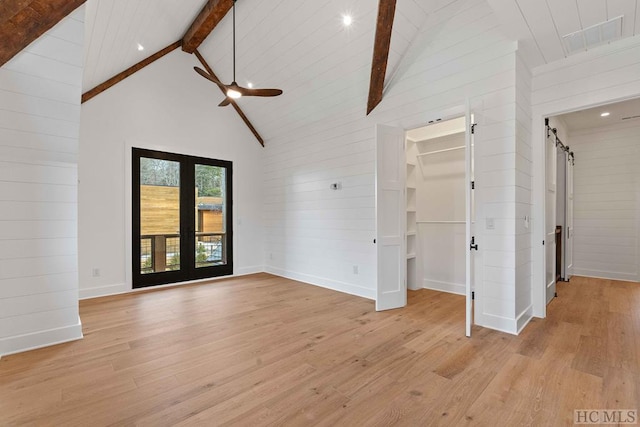 unfurnished living room featuring french doors, light wood-type flooring, beam ceiling, a barn door, and high vaulted ceiling