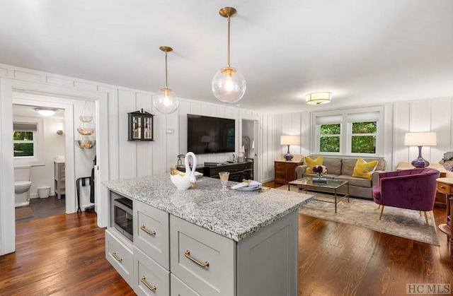 kitchen with light stone counters, a center island, stainless steel microwave, dark hardwood / wood-style flooring, and pendant lighting