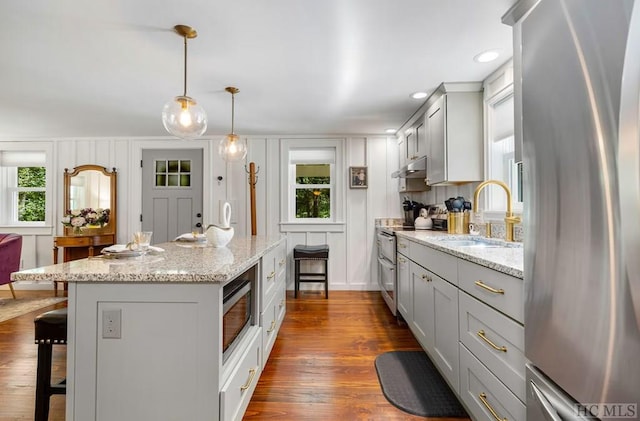 kitchen with sink, light stone counters, a center island, pendant lighting, and stainless steel appliances