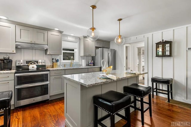 kitchen with sink, a kitchen breakfast bar, pendant lighting, stainless steel appliances, and a kitchen island with sink