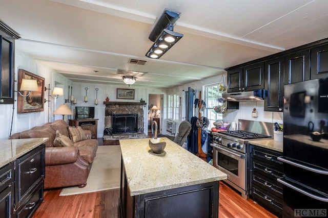 kitchen featuring a kitchen island, dark hardwood / wood-style flooring, high end stainless steel range, light stone counters, and black fridge