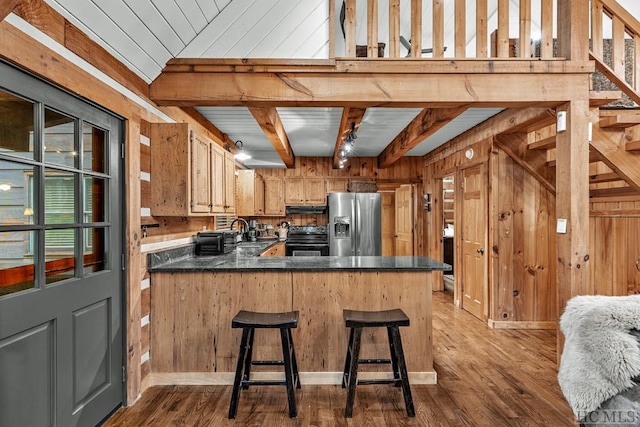 kitchen featuring kitchen peninsula, stainless steel fridge, black electric range, wood walls, and beamed ceiling