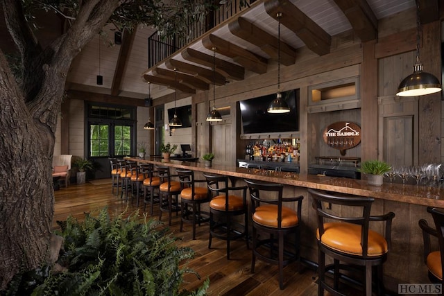 bar with dark hardwood / wood-style floors, beamed ceiling, wooden walls, and hanging light fixtures