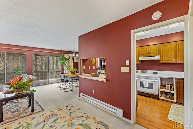 kitchen with an inviting chandelier, decorative light fixtures, baseboard heating, light colored carpet, and wall oven