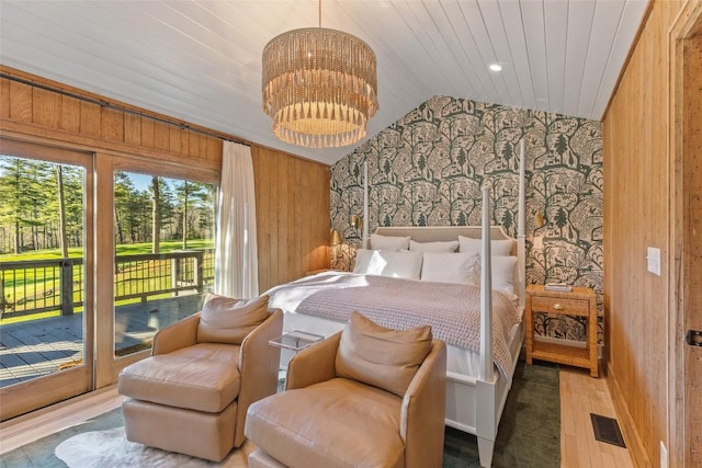 bedroom with wooden walls, access to outside, visible vents, and wood finished floors