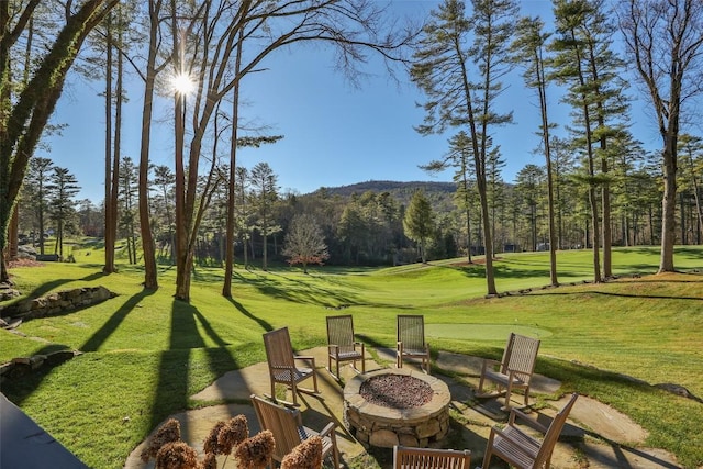view of property's community featuring a lawn, a fire pit, and a forest view