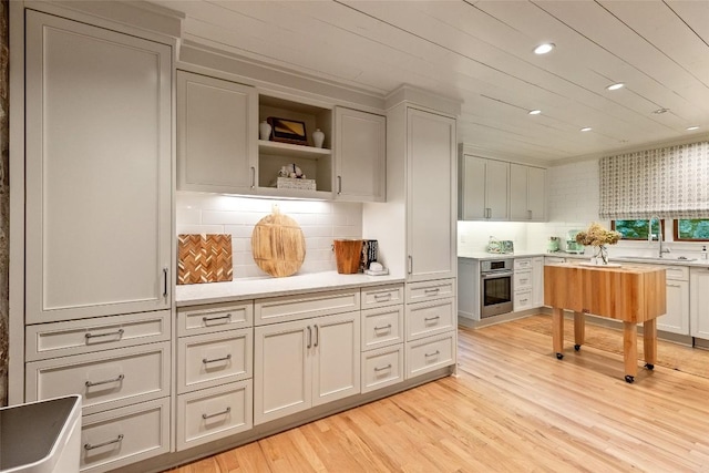 bar featuring a sink, stainless steel oven, light wood-style flooring, recessed lighting, and tasteful backsplash