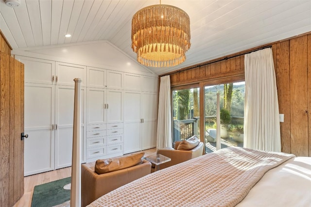 bedroom featuring a chandelier, access to exterior, light wood-type flooring, lofted ceiling, and wooden walls