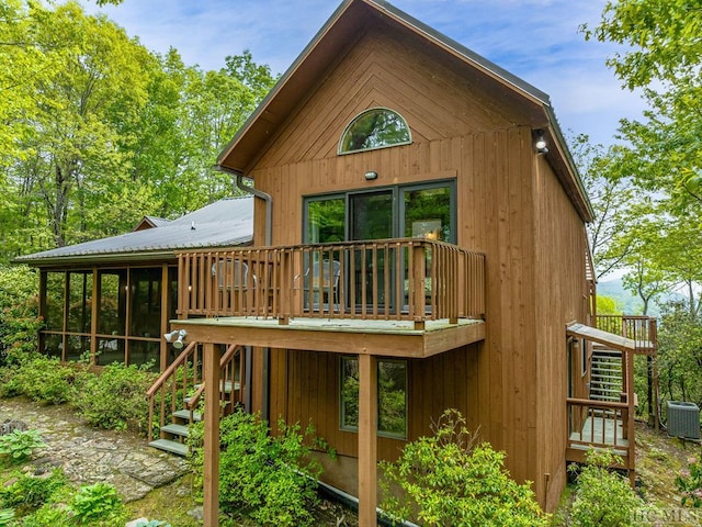 back of property with a wooden deck, central air condition unit, and a sunroom