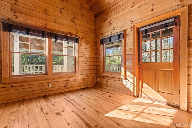 interior space with vaulted ceiling, light hardwood / wood-style floors, and wood walls