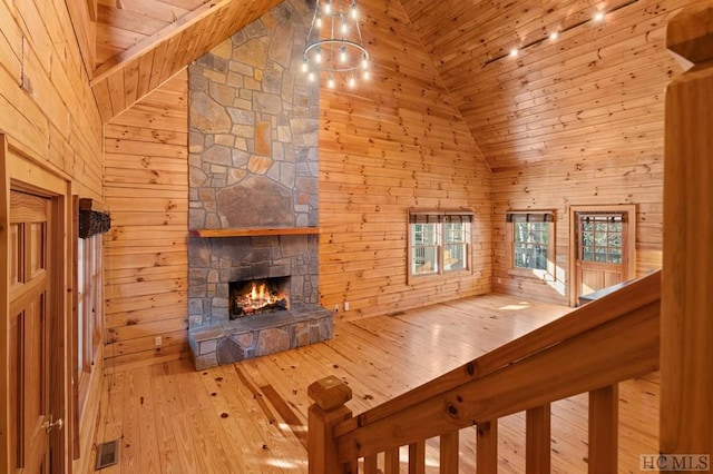 unfurnished living room featuring wooden walls, high vaulted ceiling, and a stone fireplace